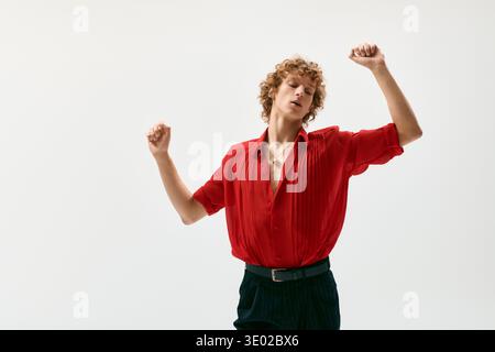 Un jeune homme aux cheveux bouclés affiche son style dans une chemise rouge vif tout en dansant. Banque D'Images