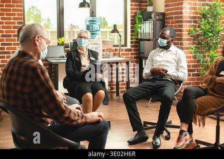 Thérapeute femme à la retraite dirigeant une séance de counseling de groupe, ayant des moments de conversation honnête entre les participants. Femme âgée avec presse-papiers donnant des conseils de santé mentale aux patients à la thérapie. Banque D'Images