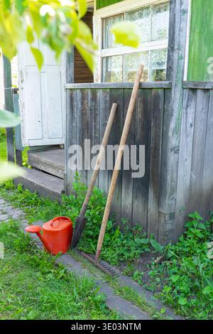 Hangar rustique, maison d'outils d'été avec des outils de jardin et arrosoir dans une végétation luxuriante Banque D'Images