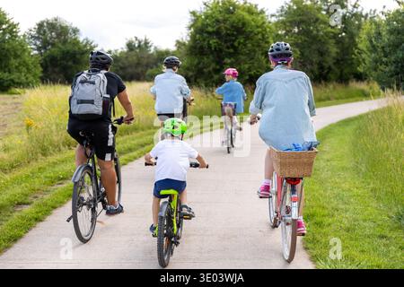 Famille enfants cyclistes chemin de campagne pavé verdoyant des arbres de prairie pendant la lumière chaude du jour d'été. Style de vie actif en plein air, liberté de loisirs Banque D'Images