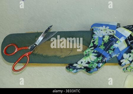 Image détaillée de Cobbler réparant des chaussures en tissu floral à l'atelier. Scène d'atelier montrant Chaussure ajustant Sandale en tissu floral sur la semelle intérieure avec Banque D'Images