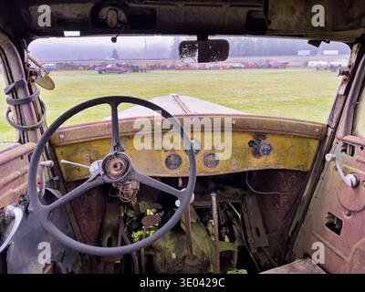 Un gros plan sur le volant et le tableau de bord d'un vieux camion rouillé avec une vue à travers le pare-brise d'une rangée de véhicules mis à la jonque dans le dis Banque D'Images