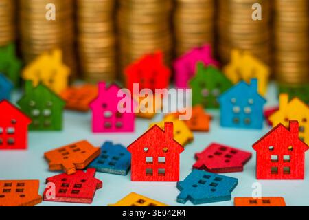 Figurines de maison en bois lumineux avec des pièces d'or empilées en arrière-plan symbolisant l'investissement immobilier et la croissance du marché du logement Banque D'Images