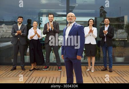 Chef d'entreprise senior confiant debout sur le toit avec l'équipe applaudissante Banque D'Images