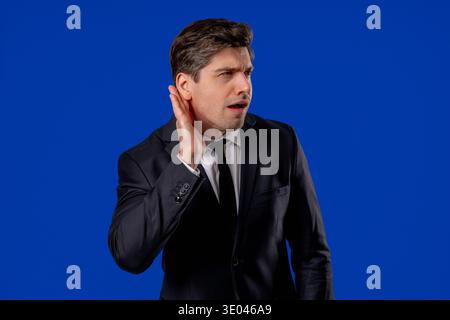 Homme d'affaires mature pointant vers l'oreille avec le visage confus, signalant qu'il ne peut entendre Banque D'Images