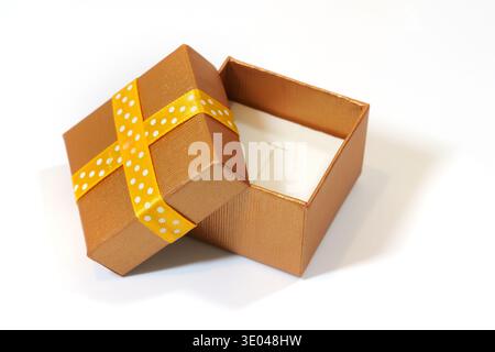Ouvrez la petite boîte cadeau avec couvercle et ruban à pois jaunes sur fond blanc, gros plan à angle élevé de l'emballage cadeau en bronze pour bijoux ou bague, surp Banque D'Images