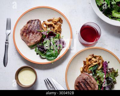 Un succulent steak grillé accompagné d’une salade verte fraîche et de champignons sautés, servi sur une assiette blanche texturée. Parfait pour un régime céto satisfaisant Banque D'Images