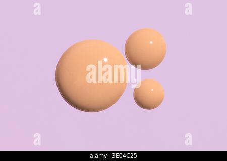 Gros plan de gouttes de fond de teint liquide beige sur un fond de lavande pastel. Idéal pour les matériaux promotionnels de beauté et de soin de la peau, mettant en valeur Smooth te Banque D'Images