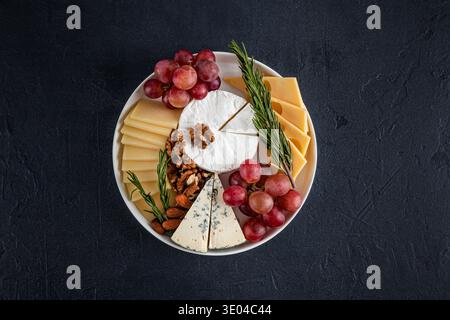Un plateau de fromages magnifiquement arrangé présente une variété de fromages, y compris doux et bleus, garnis de raisins frais, de noix croquantes et aromatiques Banque D'Images