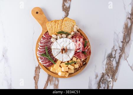 Un plateau de fromages magnifiquement arrangé avec une variété de fromages, de viandes tranchées, de noix et de craquelins sur une planche de bois ronde. Parfait pour les points d'accès élégants Banque D'Images