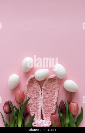 Oeufs de Pâques avec oreilles de lapin et tulipes sur fond rose. Composition des vacances de printemps Banque D'Images