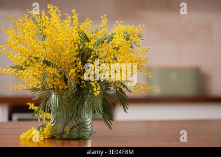 Belle fleur de mimosa jaune dans le vase en verre vert moderne, concept de décoration printanière dans l'intérieur de la cuisine moderne. La composition de printemps confortable est Banque D'Images
