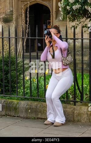 Jeune femme attirante prenant une photo à l'aide d'un grand appareil photo reflex numérique ou bridge dans le centre-ville d'Oxford, Oxfordshire, Angleterre, Royaume-Uni Banque D'Images