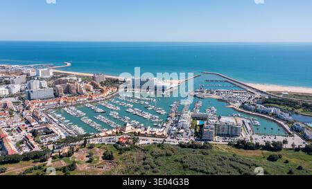Les gens visitent la marina de Vilamoura au Portugal pour profiter des bateaux, des restaurants et de la plage sous la lumière du soleil par temps clair en Algarve Aerial Banque D'Images
