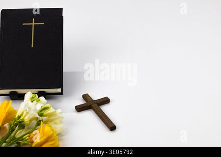 Sainte Bible avec croix et fleurs de printemps sur fond blanc, concept de foi chrétienne Banque D'Images