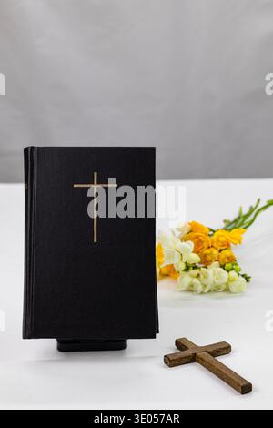 Sainte Bible avec croix et fleurs de printemps sur fond blanc, concept de foi chrétienne Banque D'Images