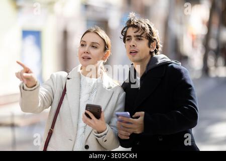 Jeune couple marchant dans la rue regardant les téléphones pour la carte de la ville Banque D'Images