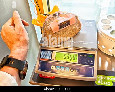 Orenburg, Russie - 22 août 2025 : le client place du pain sur une balance numérique pour le peser à la caisse d'un supermarché lors d'une visite de shopping. Banque D'Images