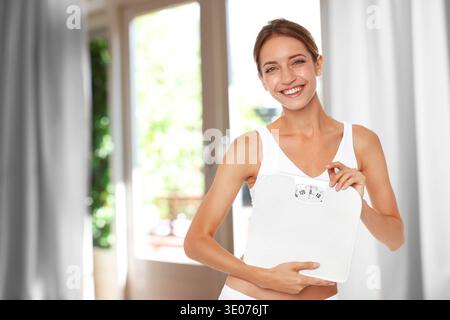 Jeune femme heureuse avec son résultat de perte de poids tenant balance de salle de bain à la maison Banque D'Images