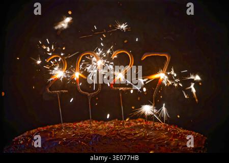 Gâteau au chocolat festif décoré de pépites colorées et de pétillants en forme de 2027 chiffres brillants dans un fond sombre. Banque D'Images