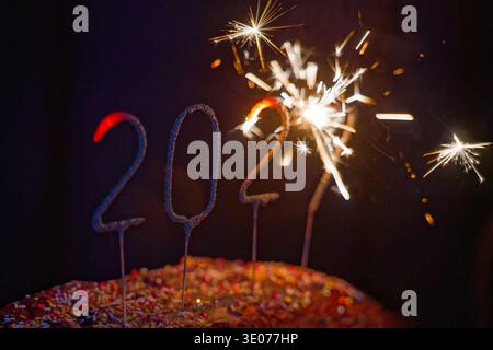 Bougies scintillantes festives en forme de 2021 brûlant brillamment sur un gâteau décoré avec des saupoudrages colorés sur un fond sombre. Banque D'Images