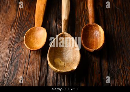 Trois cuillères en bois artisanales suspendues sur une surface en bois texturée. Décor de cuisine rustique, ustensiles traditionnels, matériau naturel, style vintage Banque D'Images