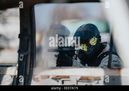 Jeu de tir de paintball en masque vise à travers une fenêtre avec un pistolet de paintball prêt Banque D'Images