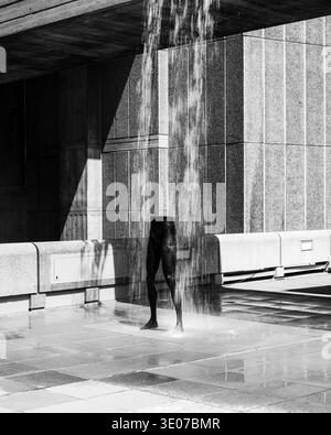 Londres - 07 09 2022 : une sculpture d'une personne se tient sous un plan d'eau dans un cadre urbain extérieur. L'eau coule autour de la figure, créatine Banque D'Images