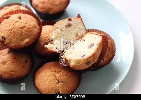Gros plan sur des muffins aux raisins faits maison avec un muffin tranché montrant de la miette tendre et des raisins secs, des pâtisseries fraîchement cuites dans des doublures en papier Banque D'Images