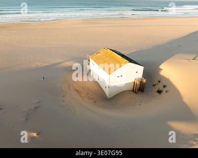 Costa da Caparica, Portugal - 29 janvier 2025 : vue aérienne d'une maison blanche solitaire sur la plage, les ombres s'étendent sur le sable doré vers le reste Banque D'Images
