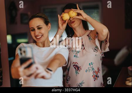 Deux amis prenant un selfie ludique avec des citrons à la maison, souriant et s'amusant ensemble Banque D'Images