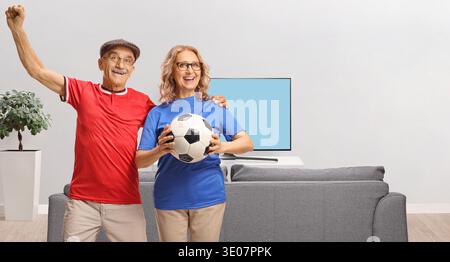 Couple de personnes âgées acclamant pour un match de football à la maison Banque D'Images