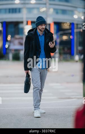 Homme d'affaires marchant à travers un passage de ville vérifiant son téléphone tout en portant une mallette Banque D'Images