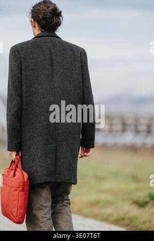 Personne marchant sur un chemin dans un manteau sombre portant un sac rouge Banque D'Images
