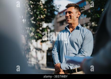Homme d'affaires confiant sourit tout en se tenant dehors dans une chemise bleu clair Banque D'Images
