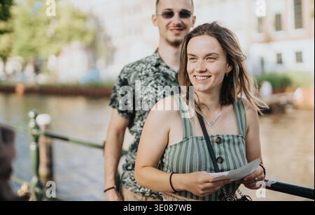 Deux amis souriants sur un pont de canal à Amsterdam profitant d'une promenade ensoleillée dans la ville Banque D'Images