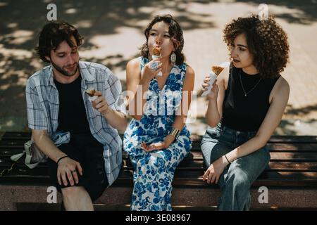 Trois amis apprécient la crème glacée sur un banc de parc dans un après-midi ensoleillé en plein air Banque D'Images