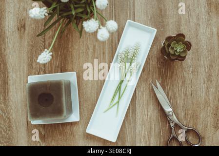 Vue aérienne d'une bougie avec un bouquet de jacinthes de raisin blanc (muscari), des cactus miniatures et une paire de ciseaux sur une table en bois Banque D'Images