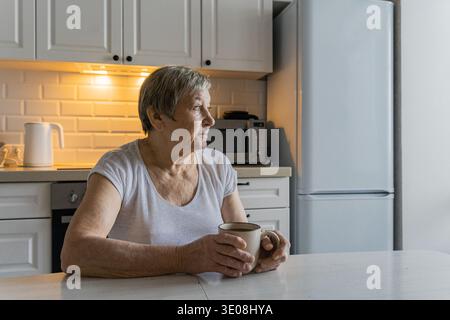 Femme âgée buvant du café contemplant dans la cuisine Banque D'Images