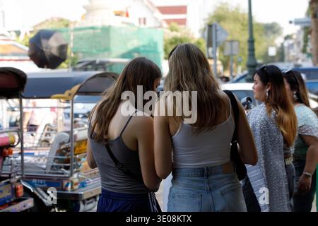 Deux femmes touristes debout ensemble, personne tenant un smartphone en ville, utilisation quotidienne de la technologie, vue arrière, à Maha Rat Road. Banque D'Images