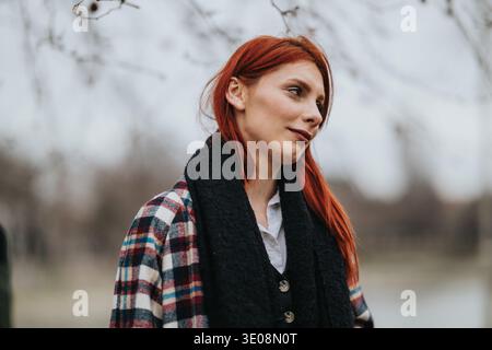 Femme aux cheveux rouges en manteau à carreaux portrait extérieur avec écharpe, regardant réfléchi Banque D'Images