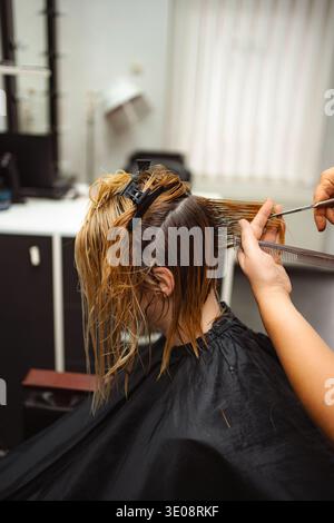 Coiffeur coupant les cheveux mouillés du client féminin dans le salon Banque D'Images