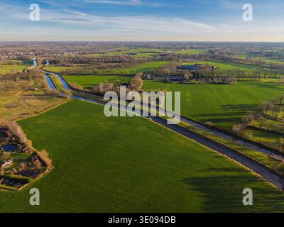 Vue aérienne d'un paysage hollandais pittoresque avec un long canal traversant des champs verdoyants et des prairies. Campagne rurale aux pays-Bas sous Banque D'Images