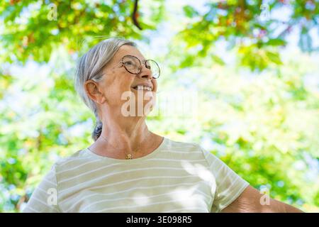 Portrait de la tête photographié en gros plan d'une femme d'âge moyen appréciant et se relaxant debout dans la nature au parc en plein air. Vieille femme souriante joyeuse Banque D'Images