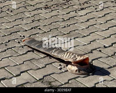 Butée de pneu endommagée sur une chaussée en béton avec ombres projetées par la lumière du soleil et gravier meuble visible. Photo mobile Banque D'Images