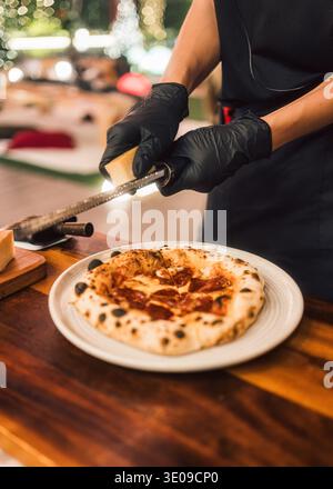 Pizza pepperoni au levain maison avec chef râpant du fromage parmesan frais sur une table en bois dans la pizzeria Banque D'Images