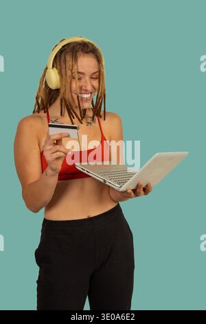 Jeune femme avec des dreadlocks souriant, tenant une carte de crédit et utilisant un ordinateur portable pour le commerce électronique Banque D'Images