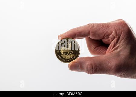 Main de l'homme tenant la pièce d'or Krugerrand, antilope springbok, détail, fond blanc, image symbolique, pièce de monnaie d'investissement, retraite, fiscalité Banque D'Images