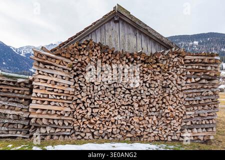 Bûches de bois de chauffage empilées devant un hangar en bois rustique dans les montagnes alpines enneigées Banque D'Images