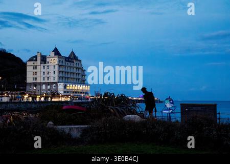 Les lumières du Grand Hôtel et de la jetée brillent dans la lumière sombre de la soirée à l'horloge florale sur le front de mer de Llandudno, dans le nord du pays de Galles. Banque D'Images